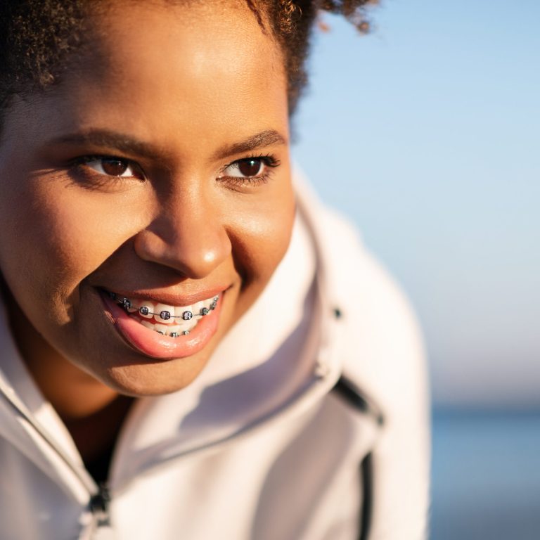 Closeup Portrait Of Smiling Young Black Female Athlete Resting Outdoors After Training, Motivated Sporty African American Woman Wearing Wireless Earphones And Dental Braces Looking Away And Smiling